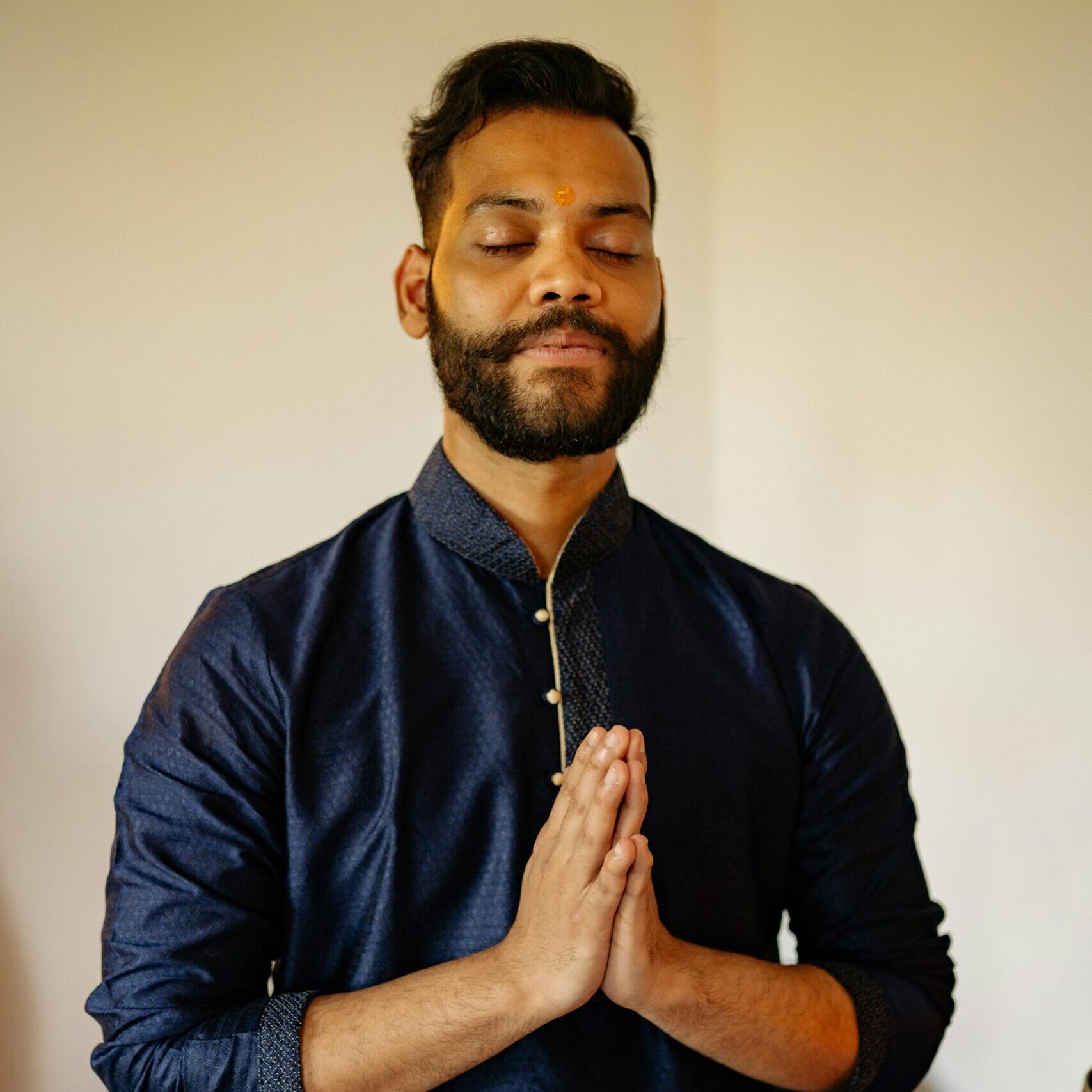 A man in traditional Indian attire with closed eyes in a prayer pose.
